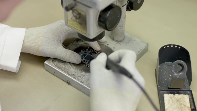 Technician in the laboratory looking into a microscope and solde