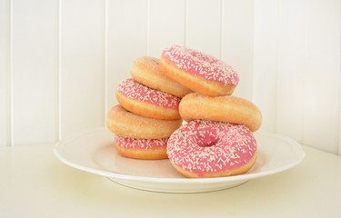Assorted pink donuts on a plate. White painted wooden planks on background