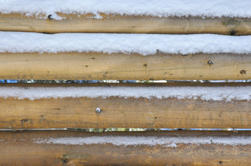 Wooden wall made of round logs. Under the snow