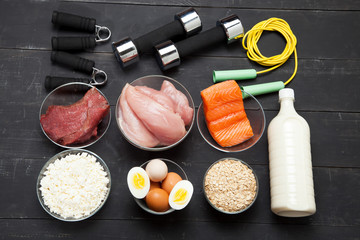 Proteins and dumbbells. Fish, cheese, eggs, meat, chicken  heart on a black wooden background