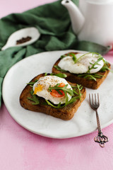 Toast with poached Egg, arugula and cherry tomatoes on a pink background (close-up)