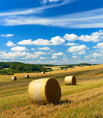 Stoppelfeld mit Strohballen, Sommerlandschaft unter blauem Himmel, sanfte Hügel