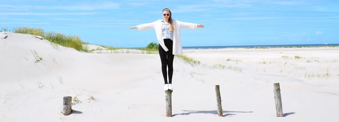 junge Frau balanciert auf einem Holzpfahl am Meer, Nordseeinsel Rømø, Dänemark