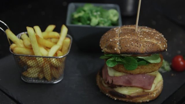 Hand of a cook placing a basket of fench fries on a plate, next to a hamburger