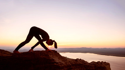 Young woman with yoga posture on the mountain at sunset.