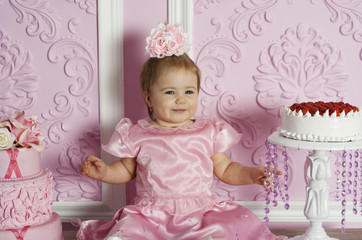 Fototapeta premium Portrait of cute baby girl in pink dress with gourmet cakes. Kid looking in camera