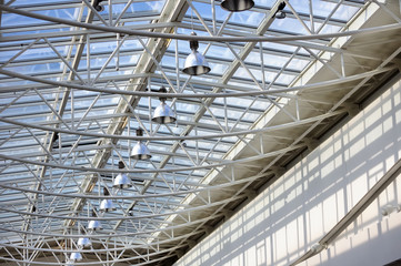 Fragment of modern building with roof made of glass and metal with row of lamps against blue sky background
