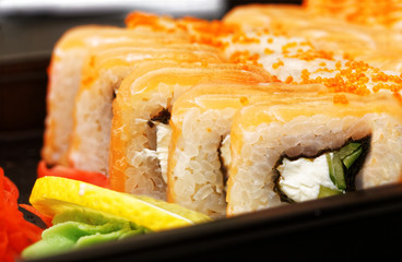 Closeup fresh maki sushi with gari ginger, wasabi and lemon on black plate. Shallow focus.