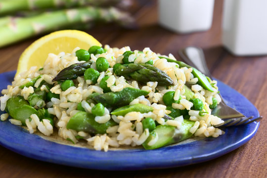 Green asparagus, pea, parsley and brown rice risotto served on plate, photographed on dark wood with natural light (Selective Focus, Focus on the asparagus heads on the top of the dish)