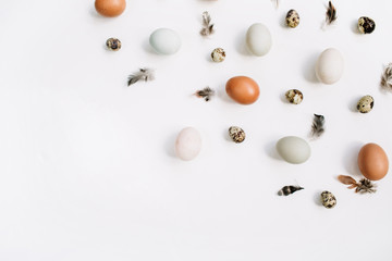 White and brown Easter eggs, quail eggs and feathers on white background. Flat lay, top view. Traditional spring concept.