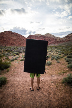 Person carrying black rectangular photography reflector by rock formations 