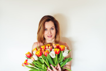 Happy young red hair woman holding big bouquet of red yellow tulips standing against white background