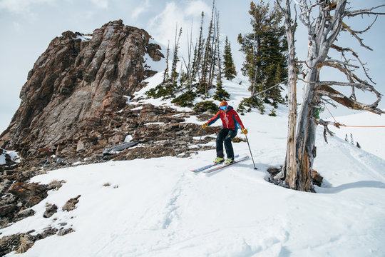Skier descending snowy slope by rock formation and trees 
