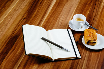 Notizbuch, Croissant und Kaffeetasse auf Holztisch