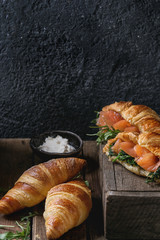 Croissant with smoked salted salmon, spinach and arugula served with bowl of cream cheese over dark old wooden table. Copy space