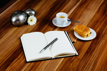 Notizbuch, Croissant und Kaffeetasse auf Holztisch