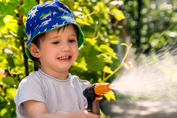 Little happy baby in the garden with a sprinkler for watering the garden, spoiled and showing tongue