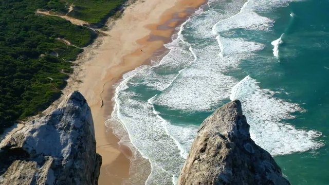 view from top of rocks to sandy beach and waves
