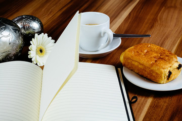 Notizbuch, Croissant und Kaffeetasse auf Holztisch
