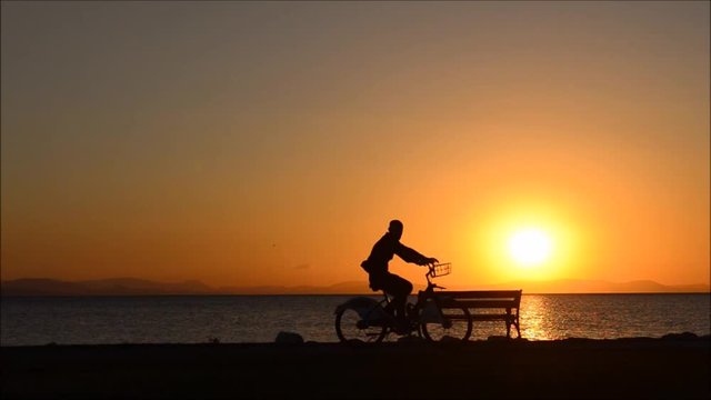 Man riding bicycle near the sea at sunset.