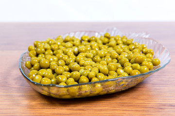 Canned green peas in a glass plate in the form of fish close-up on the table.