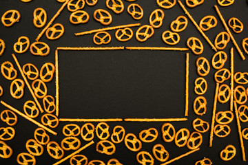Background texture of salted salty pretzels and mini sticks in the traditional form of the hinge assembly on a black background. Space for text.