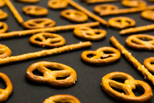 Background texture of salted salty pretzels and mini sticks in the traditional form of the hinge assembly on a black background.