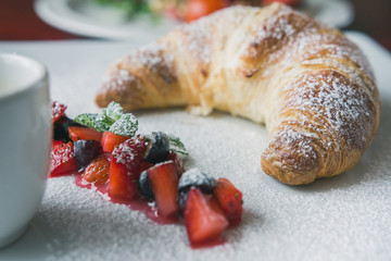 Breakfast dessert - pcroissant with powdered sugar, fruit and sauce, close up