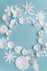 Round frame with white paper flowers on blue background. Cut from paper.