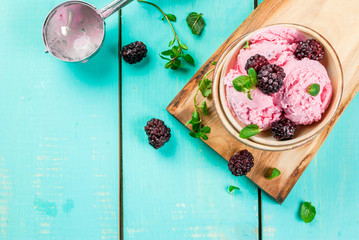 Berry ice cream in a small ice-cream bowls with blackberries and mint on a table, with berries and mint leaves and spoon on blue wooden table.