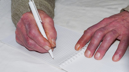 Closeup of the wrinkled hands of an old caucasian man holding pen and paper