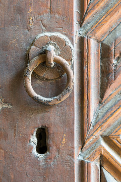 Closeup of rusted ring door knocker over an aged decorated wooden door