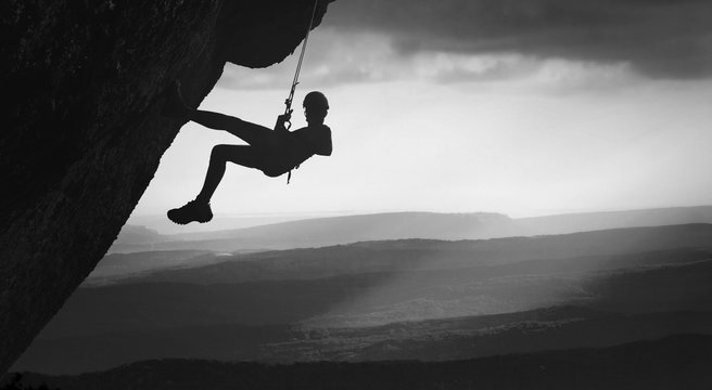 Climber on a cliff against misty mountains. Black and white