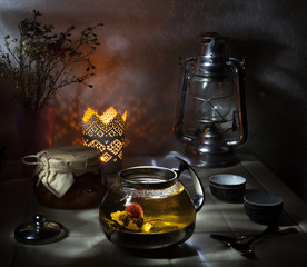 Glass teapot with blooming green tea on white table and dark background still life