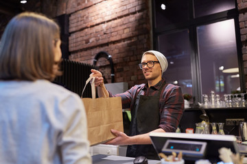 woman taking paper bag from seller at cafe