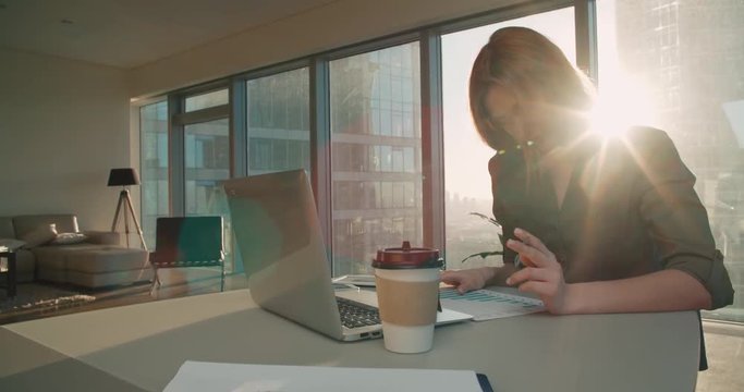 Young business woman sitting at a desk in a modern office in a skyscraper works, create a presentation, glare of the sun, steadicam shot