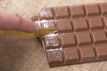 Hand with knife cutting chocolate with icing sugar. Horizontal shoot.