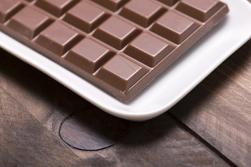 Chocolate tablet on white tray on wooden table. Isolated. Horizontal shoot.