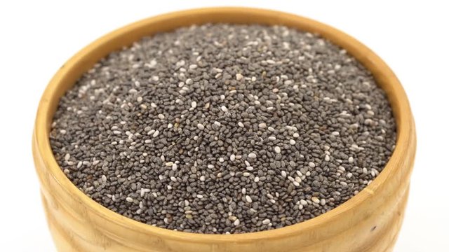 Chia seeds in a loopable rotating wooden bowl making one full round seen obliquely from above on white background