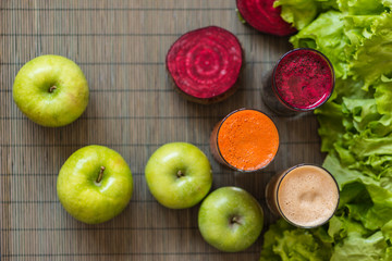 three glasses of different fresh juice. Beet, carrot and apple juices on grey wood background