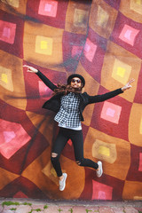stylish young woman in hat jumping near the wall with graffiti 