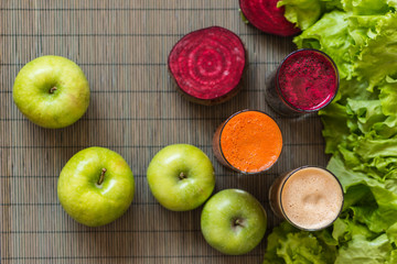 three glasses of different fresh juice. Beet, carrot and apple juices on grey wood background