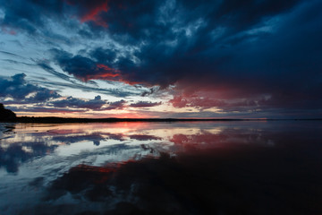 Naklejka na ściany i meble Beautiful sunset on the lake, the clouds reflected in the water. Surface on the lake. Russia, Karelia. Wide photo