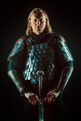 Powerful blond knight with the sword on the dark background