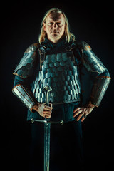 Powerful blond knight with the sword on the dark background