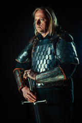 Powerful blond knight with the sword on the dark background