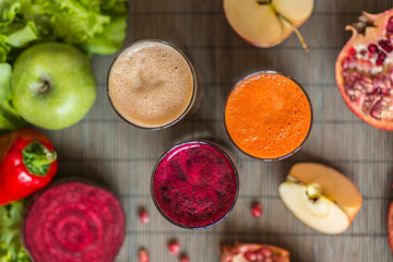 three glasses of different fresh juice. Beet, carrot and apple juices on grey wood background