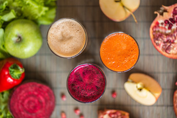three glasses of different fresh juice. Beet, carrot and apple juices on grey wood background