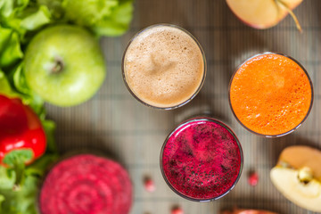 three glasses of different fresh juice. Beet, carrot and apple juices on grey wood background