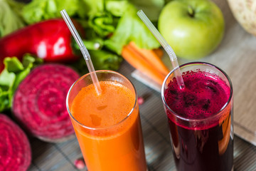 two glasses of different fresh juice. Beet and carrot juices on grey wood background